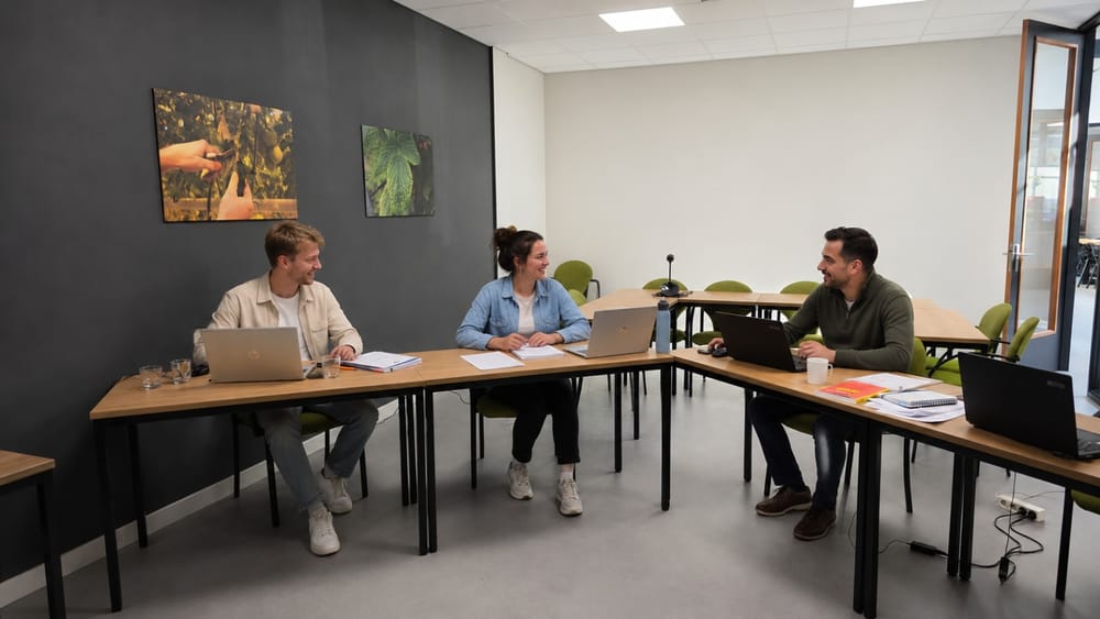 Drie cursisten overleggen met hun laptops in een trainingsruimte