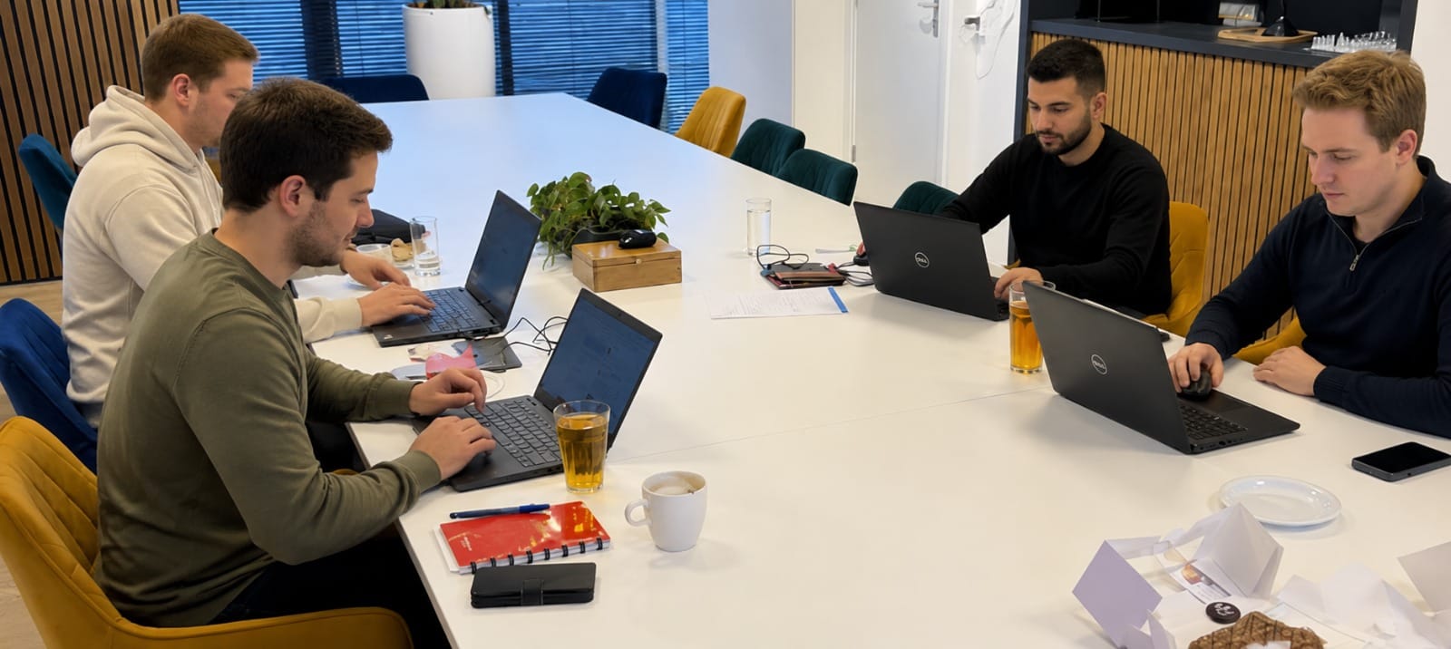Vier cursisten werken aan hun eigen casus op laptops rond een grote tafel