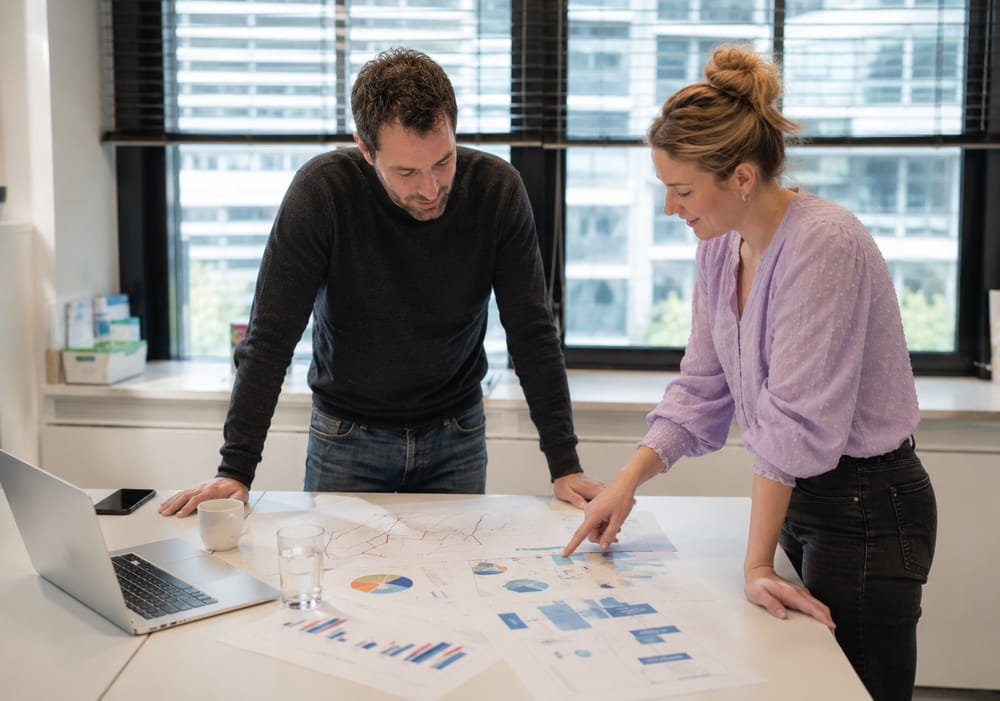 Twee cursisten bespreken analytics-rapporten met grafieken op tafel tijdens de Google Analytics-cursus