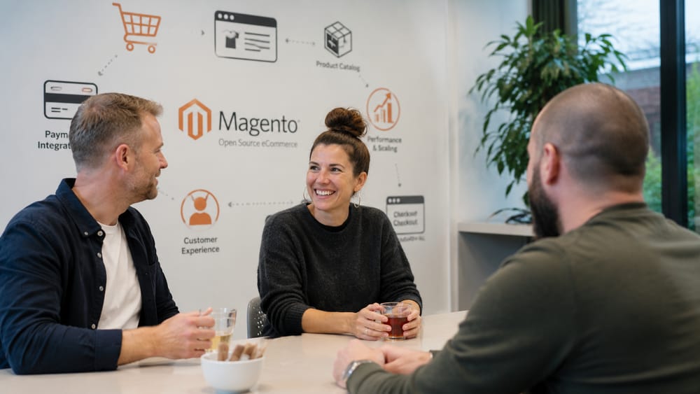 Cursisten in gesprek voor een wand met het Magento-logo en e-commerce-illustraties tijdens de Magento Webshop-cursus